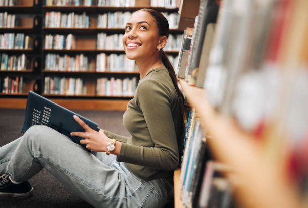 istock Student, library and smile for reading books in learning, education or knowledge at university. Happy woman smiling enjoying book read, story or study in research for assignment or project at campus 1470038809