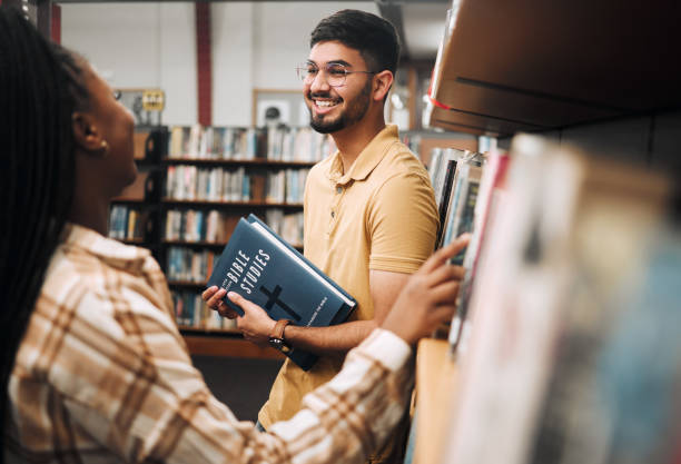 istock Talking students, bonding and library bookshelf on school, college and university campus for education, learning and religion studying. Smile, happy man and black woman friends with textbook research 1470038832