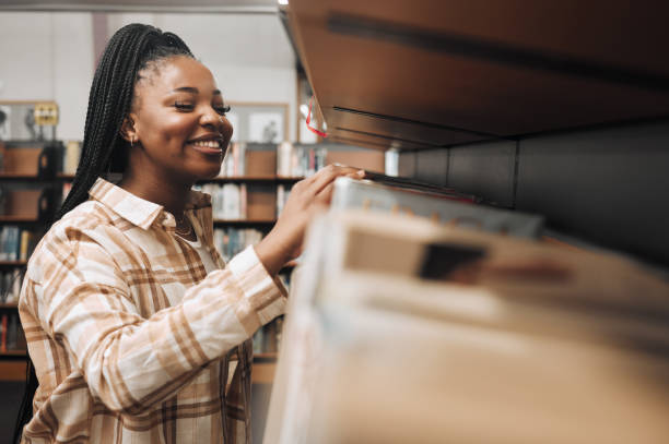 istock Student, checking or library bookshelf on school, college or university campus for education, learning or studying. Smile, happy or excited black woman in textbook search, research or retail shopping 1470038839