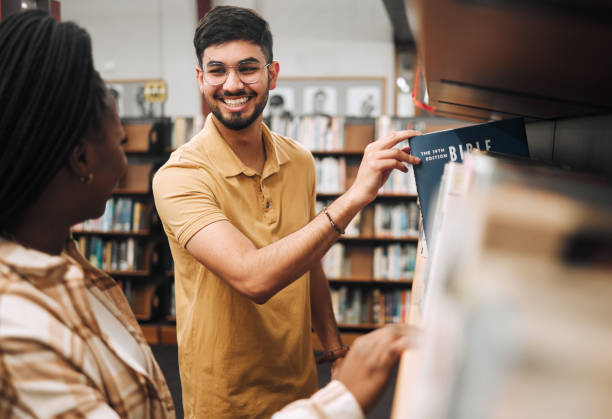 istock Studying religion, research and students in library, college bookshelf and happy with knowledge on campus. Smile, choice and couple of friends with scholarship for learning, education and university 1470038841