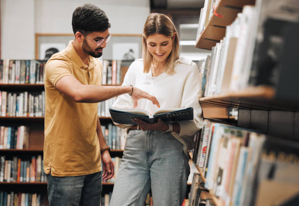 istock Students, library and discussion for man, woman or book for knowledge, learning or information in university. Bookshelf, conversation and reading for college student, friends or education for success 1470038842