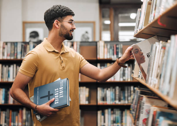 University, student or man with bible in a library to study spiritual religion knowledge, prayer or Christ bookshelf search. Smile, school or happy man in college studying or worship research in God universidad, estudiante u hombre con biblia en una biblioteca para estudiar el conocimiento de la religión espiritual, la oración o la búsqueda de la estantería de cristo. sonríe, escuela u hombre feliz en la universidad estudiando o adorando la inves