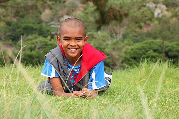 Young ethnic boy lying in grass with big smile