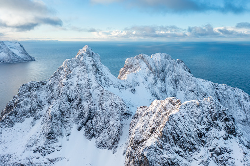 Snow covered mountain range on coastline in winter, Norway. Senja panoramic aerial view landscape nordic snow cold winter norway ocean cloudy sky snowy mountains. Troms county, Fjordgard