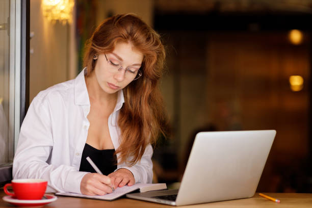 istock Young beautiful female student studying with laptop in cafe at the window 1470039794