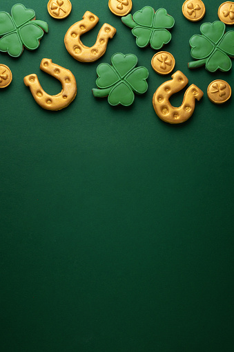 Vertical banner for St. Patrick's Day on green background. Coins, horseshoes, four-leaf clover as symbols of the holiday. Place for text. Gingerbread cookie items.