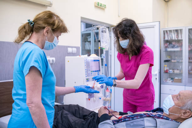 Two nurses prepare a patient for hemodialysis. Two nurses, one in blue and one in red workwear, are preparing a patient for hemodialysis - healthcare and medicine concepts. dialysis stock pictures, royalty-free photos & images