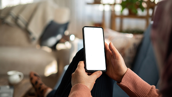 Mujer usando el teléfono con pantalla blanca mientras está acostada en el sofá de su casa, pantalla de maqueta photo