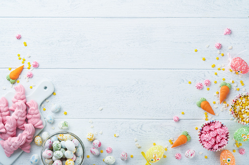 Sweet Easter concept. Sweet Easter kids holiday assortment marshmallows rabbit, chocolates easter eggs, candies, bunny, snacks on white wooden background. Flat lay Easter decoration idea. Mock up.