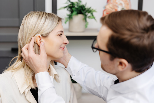 A young attractive otolaryngologist doctor gives a consultation to a female patient. A doctor explains how to wear a hearing aid to a woman.
