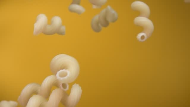 Dry Italian pasta cellentani is flying diagonally on a yellow ochre background