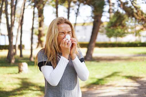 Mujer que sufre de alergia primaveral, sonarse la nariz con un pañuelo en el parque photo