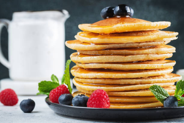 istock Delicious pancakes, with fresh blueberries, raspberry and maple syrup or honey on a dark background 1470059018