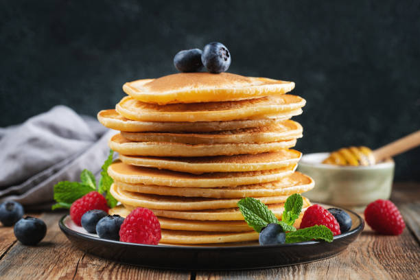 istock Delicious pancakes, with fresh blueberries, raspberry and maple syrup or honey on a dark background 1470059019