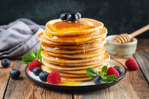 istock Delicious pancakes, with fresh blueberries, raspberry and maple syrup or honey on a dark background 1470059023
