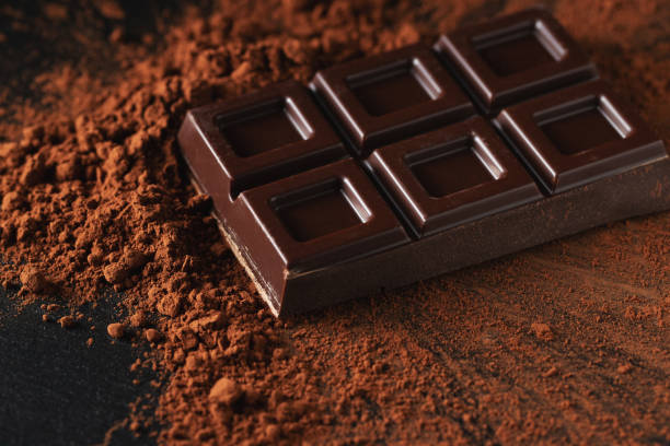 chocolate negro y con leche con nueces sobre un fondo oscuro espolvoreado con cacao en polvo. - brown chocolate candy bar close up fotografías e imágenes de stock