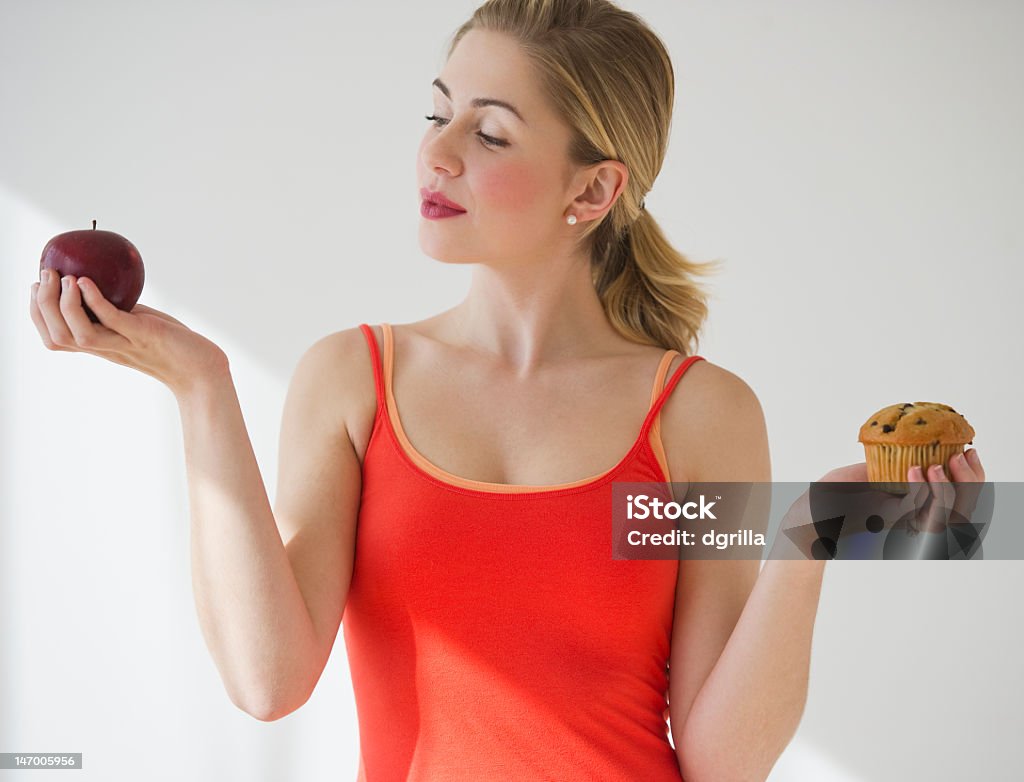 A woman holding an apple in one hand and a muffin in other female deciding between eating an apple or a muffin Adult Stock Photo