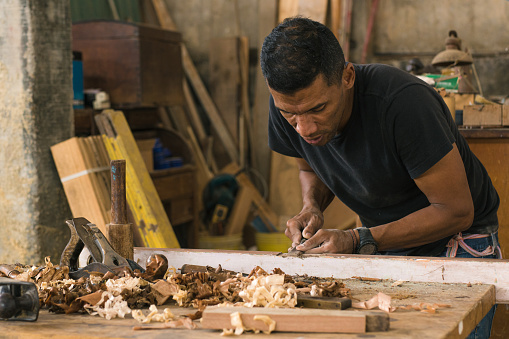 Latino worker doing his daily chores. Enterprising man doing his daily trades. carpenter using his tools to make pieces of wood. Local workshop attended by its owner. craft procedures with wood. Temporary non-agricultural jobs for immigrants with H-2B visas. Proper handling of tools. Colombian man in his workshop