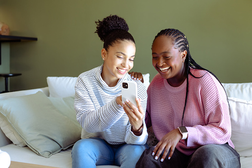 Happy African-American female friends sitting on the couch and looking at smart phone