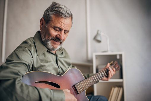 A lonely man with a beard enjoys playing the guitar at home