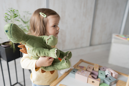One baby girl toddler playing at home with dinosaur toy, early child development and montessori concept
