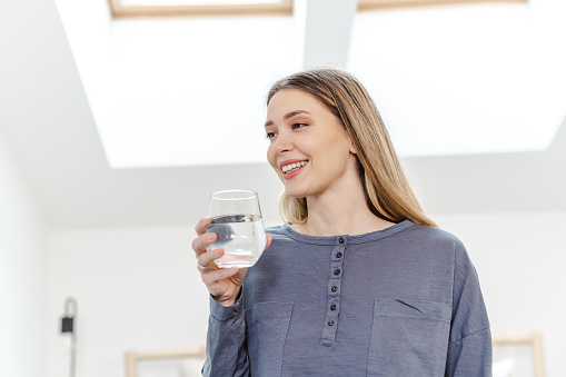 Young beautiful woman in pajamas holding a glass of water and smiling