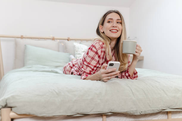 istock Young woman drinking morning coffee in bed and using smart phone 1470066860