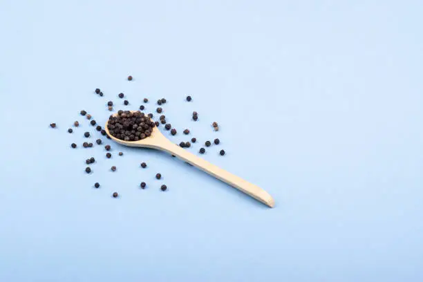 Wooden spoon with black pepper in a minimalist style. Top view. Scattered black pepper