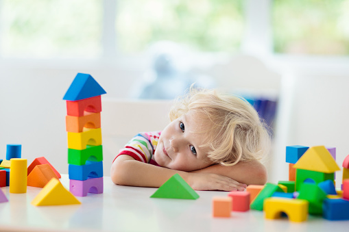 Kid playing with colorful toy blocks. Little boy building tower of block toys. Educational and creative toys and games for young children. Baby in white bedroom with rainbow bricks. Child at home.