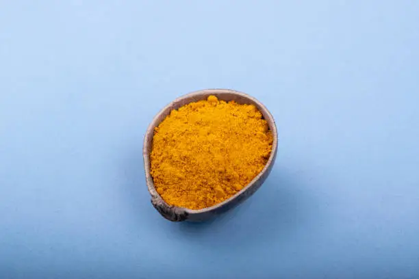 natural ground turmeric in wooden bowl in minimalist style, top view. Blue background