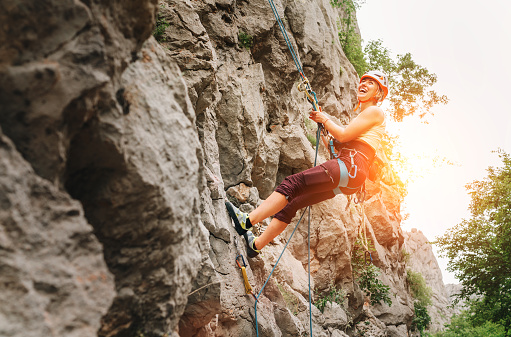 Smiling athletic woman in protective helmet and shoes climbing cliff rock wall using top rope and harness in Paklenica National park site in Croatia. Active extreme sports time spending concept