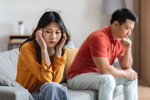 Frustrated japanese spouses after fight, upset asian man and woman sitting on couch far from each other, looking down, thinking about divorce, breakup after quarrel, home interior