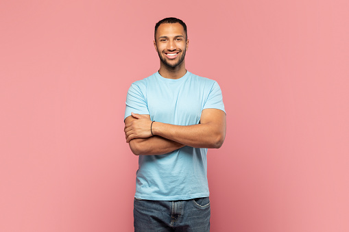 Confident man. Portrait of happy african american guy standing with folded arms and smiling, posing isolated over pink studio background. Happy casual male model looking at camera
