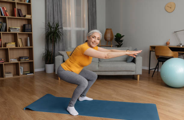 istock Active senior lady doing squats on domestic workout, training in living room and smiling at camera, copy space 1470095646
