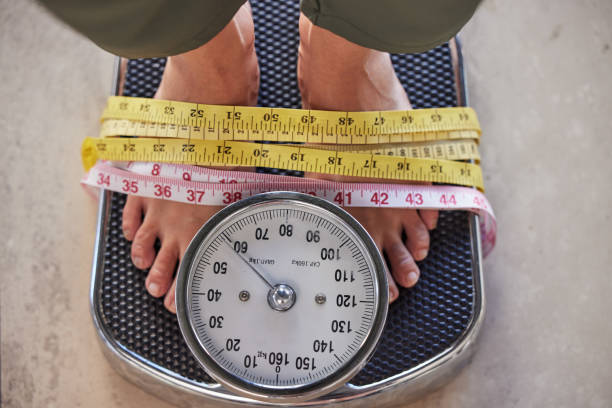 Top view, feet on scale and tape to lose weight, health and diet for wellness, balance and fitness. Obese, measure and results after training, healthy lifestyle or commitment to exercise and weighing vista superior, pies en báscula y cinta adhesiva para perder peso, salud y dieta para el bienestar, el equilibrio y el estado físico. pie, medida y resultados después del entrenamiento, estilo de vida saludable o compromiso con el ejercicio y el pesaje