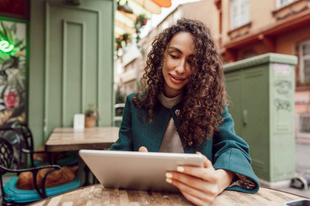 istock Beautiful curly businesswoman using digital tablet outdoors in cafe 1470096011