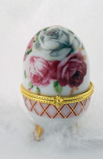 Image of a beautiful and decorative porcelain easter egg that is sitting on top of a white feather.