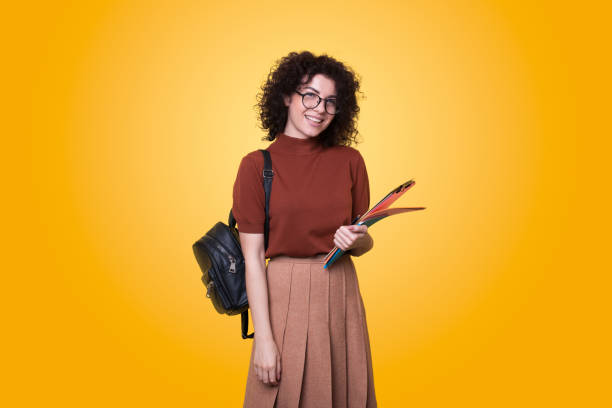 junge lockige studentin mit rucksack und brille mit büchern isoliert über gelbem hintergrund. schulbildung. moderner stil. - 6351 stock-fotos und bilder