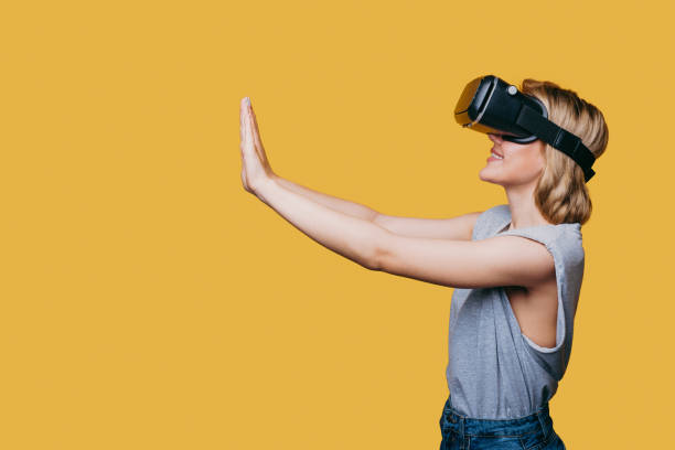 istock Happy woman getting experience using VR-headset glasses much gesticulating with hands isoalted over yellow background. Free space for text. Copy space. 1470097946
