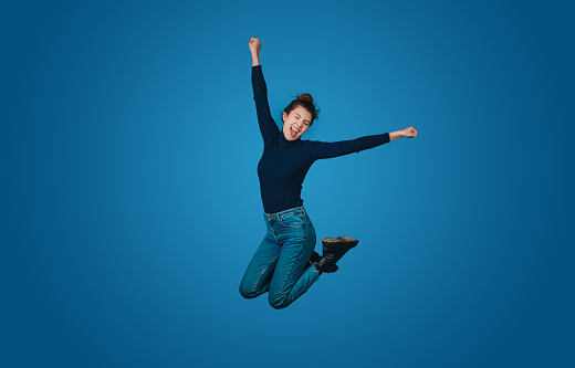 Overjoyed excited woman wear jumping high with outstretched hands isolated on blue background studio portrait. People lifestyle concept