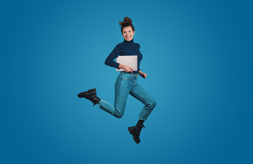 Full length body size profile of excited positive woman jumping high hold notebook isolated over blue color background