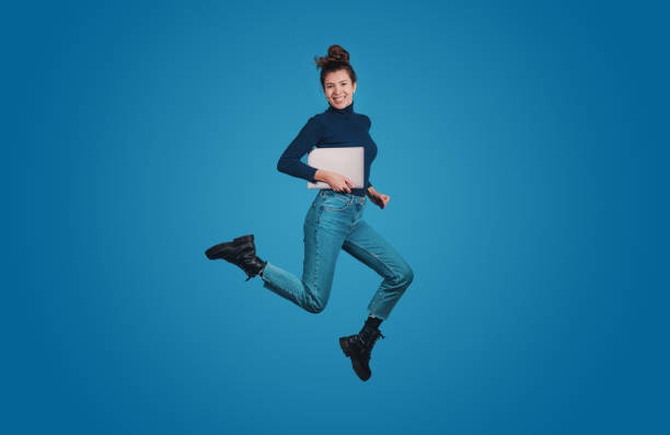 full length body size profile of excited positive woman jumping high hold notebook isolated over blue color background - job joy student computer imagens e fotografias de stock