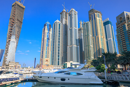 Dubai, United Arab Emirates - In view are boats and motor yachts moored on Dubai Marina; in the background are modern skyscrapers that house offices, apartments and hotels. Photo shows off a modern luxurious lifestyle that is synonymous with the Arabian Gulf city of Dubai. Photo shot in the morning sunlight against a clear blue sky; horizontal format. Note to Inspector: All boat registration numbers have been removed.