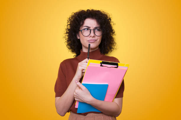 istock Thoughtful young woman student, thinking about new ideas to write an essay for homework isolated over yellow background 1470101439