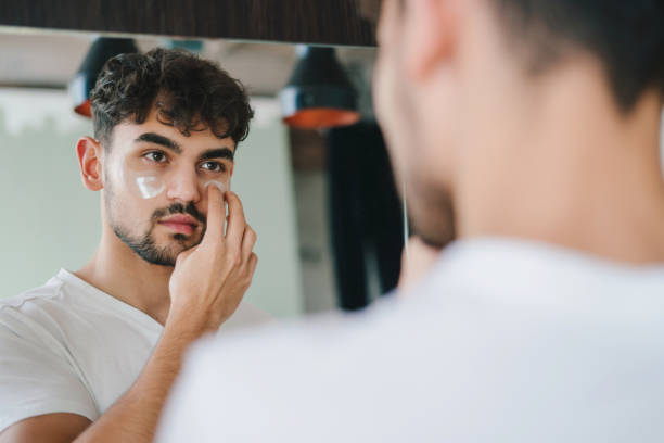 istock Portrait of handsome young man looking at his reflection in mirror, touching face, applying moisturizeron his face. Over the shoulder view. Facial skincare. Happy lifestyle. Beauty face. Beauty treatment. People lifestyle portrait. 1470101702