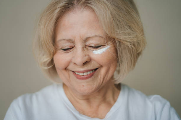 attractive smiling senior woman applying anti-aging cream to the wrinkles around her eyes in an effort to combat aging in a skincare and beauty concept. beauty portrait. facial treatment. closeup portrait. facial skincare. - senior adult fragility human eye wrinkled imagens e fotografias de stock