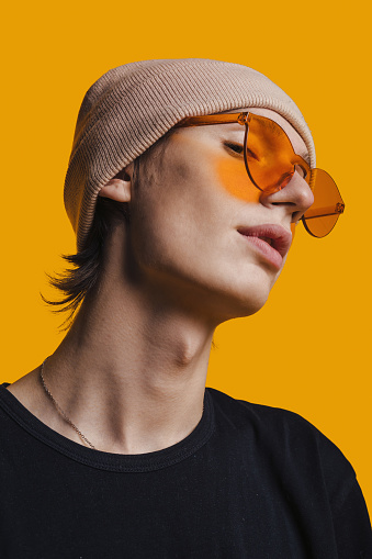 Portrait of handsome young man in hat and glasses posing over yellow background. People lifestyle portrait. Modern lifestyle. Satisfied person.
