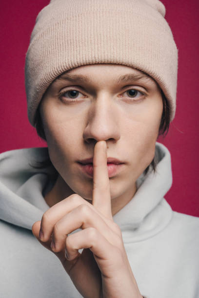istock Handsome young man wearing hat holding his finger near his lips asks for silence,isolated over pink background. Silence and secret concept. 1470105090