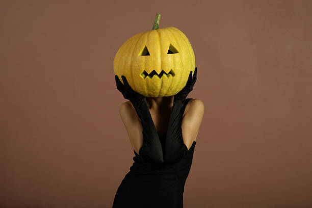 A woman dressed in black holding a pumpkin for Halloween stock photo