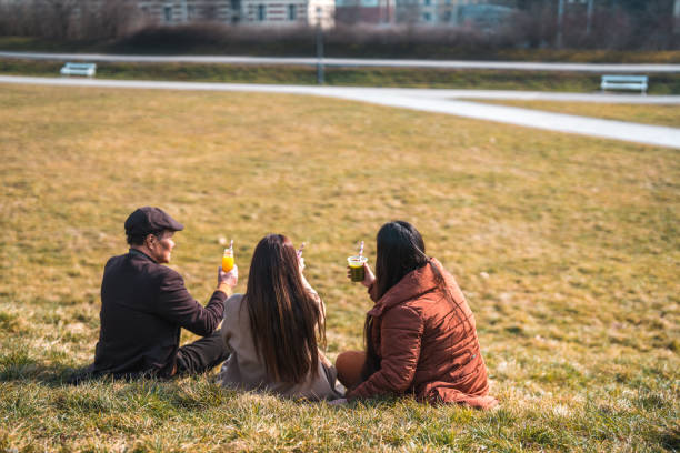 Three carefree friends relaxing on a meadow near a lake in a public park in Argentina, Buenos Aires
